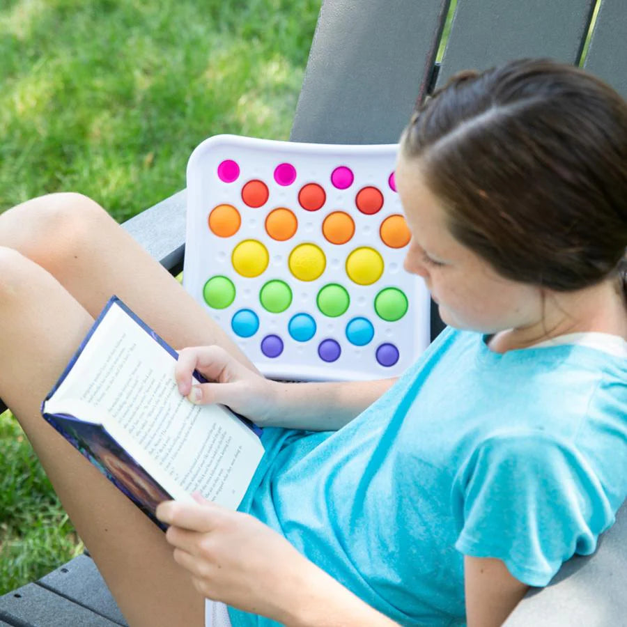 Person sitting outdoors with a book and colourful pop-it toy
