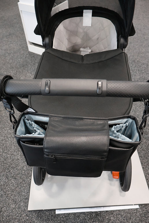 Black stroller with a bag attached on a gray floor