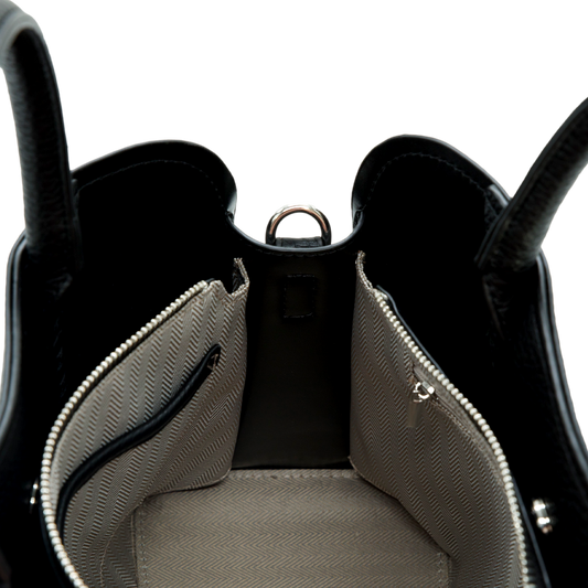 Close-up of a black vegan leather handbag with open front pocket on a white background