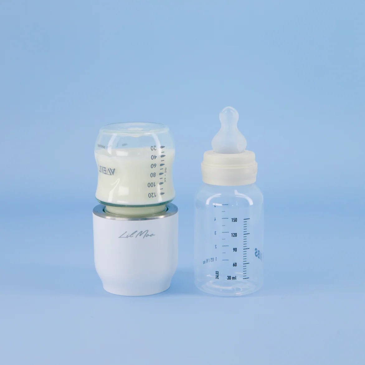 Two baby bottles with measurement markings and a Lil Moo Bottle Warmer on a light blue background