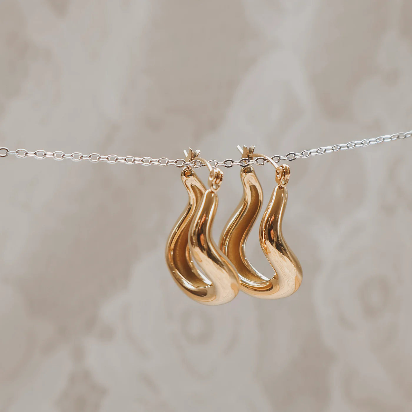 Gold earrings hanging on a silver chain on a neutral background