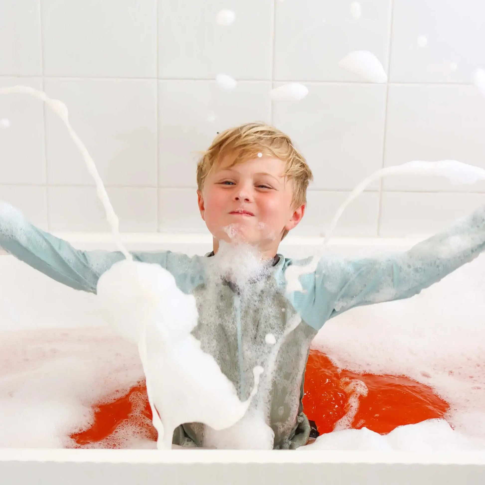 Child in a bathtub filled with Honeysticks bubbles and water, enjoying a bath.