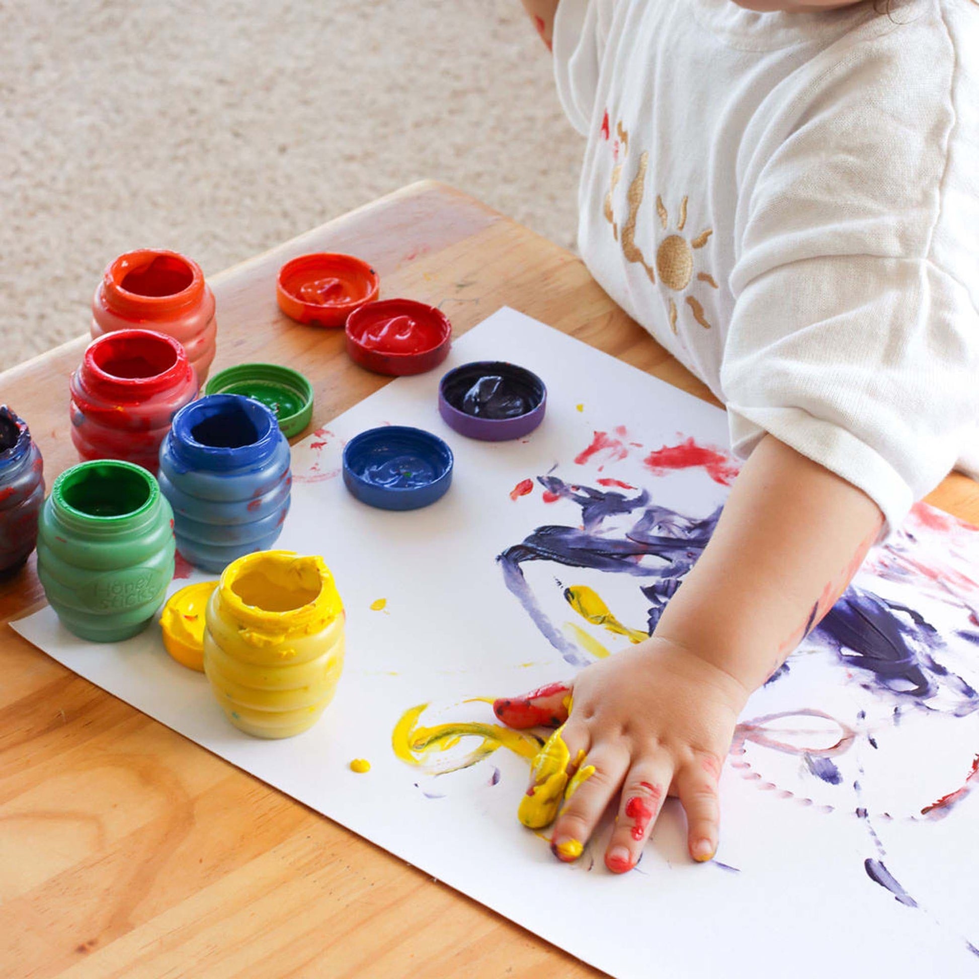 Child painting with colourful paint containers on a wooden table