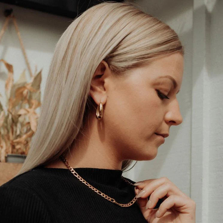 Woman wearing gold hoop earrings and a chain necklace, looking away from the camera.
